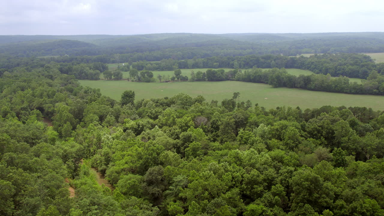 empuje aéreo sobre árboles y campos abiertos con bonitas colinas en el horizonte en el sur de missouri en un día nublado de verano