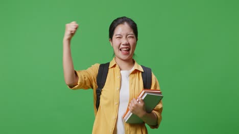 asian woman student with a backpack and some books screaming goal celebrating succeed learning in the green screen background studio