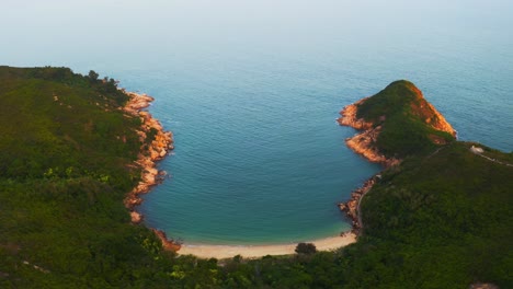 Drone-shot-traveling-forward-of-a-little-tropical-bay-with-a-beach-on-the-side-of-a-hill-during-the-day