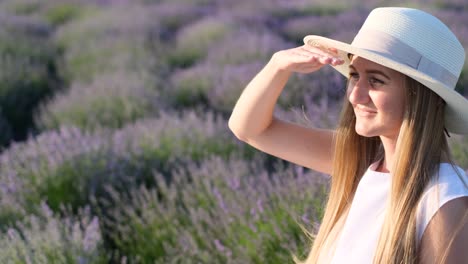 Portrait of a Blonde Woman with a White Hat in a Lavender Field in Provence France Portrait of a Blonde Woman with a White Hat in a Lavender Field in Provence France Beautiful Young Woman Looks towards the Sun Covering her Hand Sunny Day