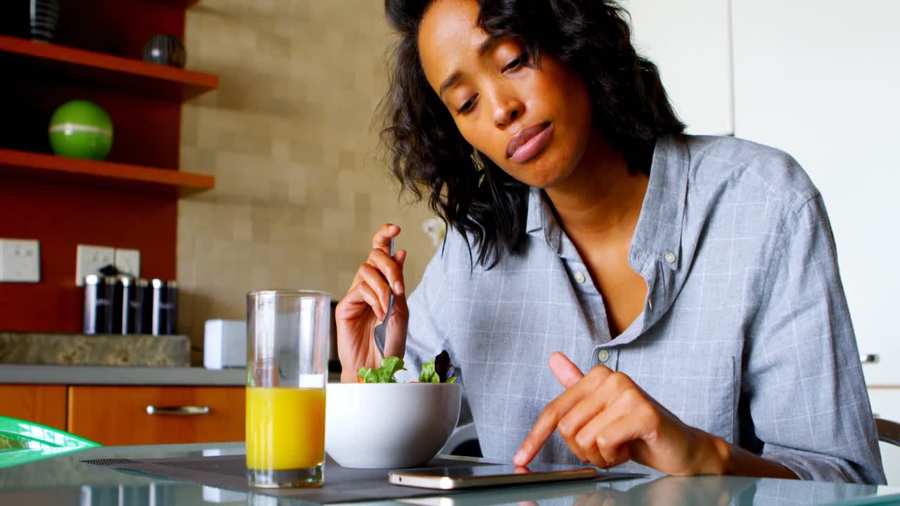 mujer usando teléfono móvil mientras come en la cocina 4k