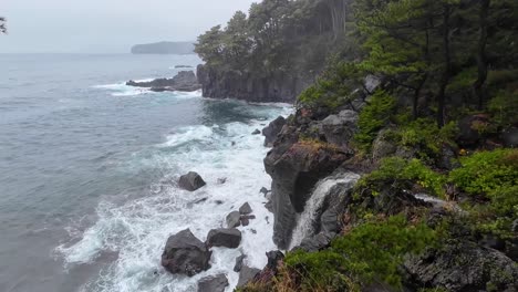 Dramatische-Küstenlinie-Mit-Starken-Wellen,-Die-An-Den-Klippen-Brechen-Und-Von-Der-Waldseite-Aus-Das-Meer-Und-Den-Ozean-überblicken,-Und-Einem-Wasserfall,-Der-Vom-Fluss-In-Den-Ozean-Fällt