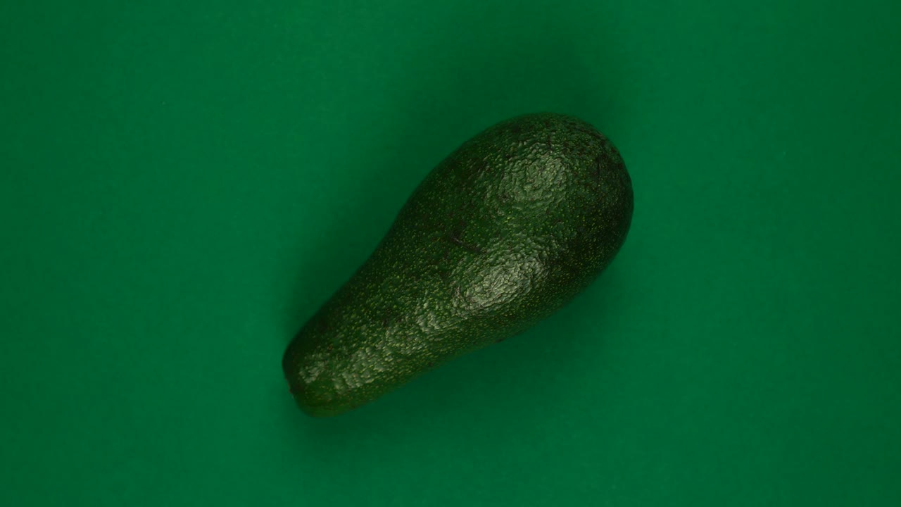 전체 아보카도 과일이 초록색 배경에 회전하고 있습니다.