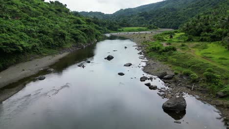 flyover shot of idyllic river in between tropical valley with lush jungles and mountains background in the philippines