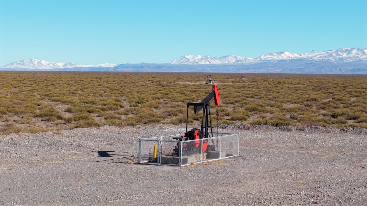 Remote oil pumpjack operates in arid plains of Mendoza, Argentina, framed by Andes mountains