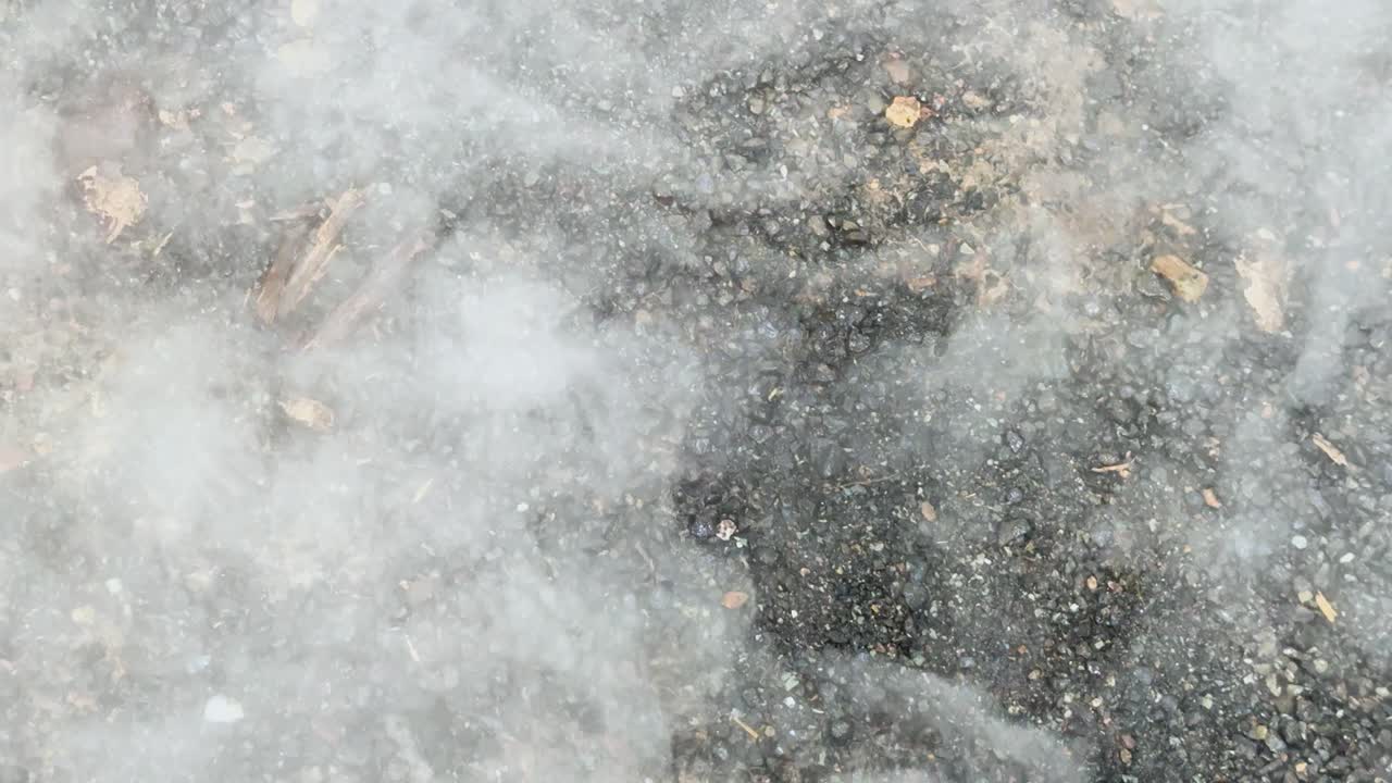 Dense white smoke drifts over gravel surface, static camera, natural daylight, outdoor environment