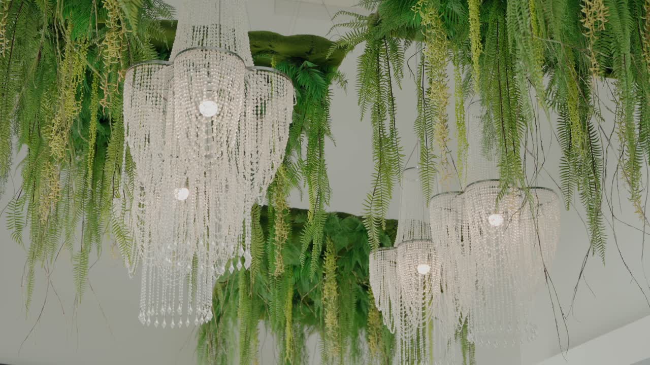 Luxurious crystal chandeliers elegantly draped with hanging ferns and green accents