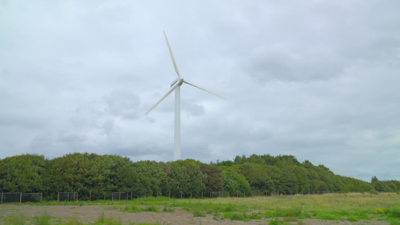 밝은 구름진 회색 하늘과 함께 황무지를 가로질러 나무 선 뒤에 풍력 터빈에 접근