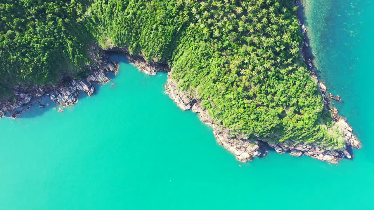 Beautiful rocky coastline of hill slopes with green vegetation of jungle washed by calm turquoise sea on tropical island in Thailand