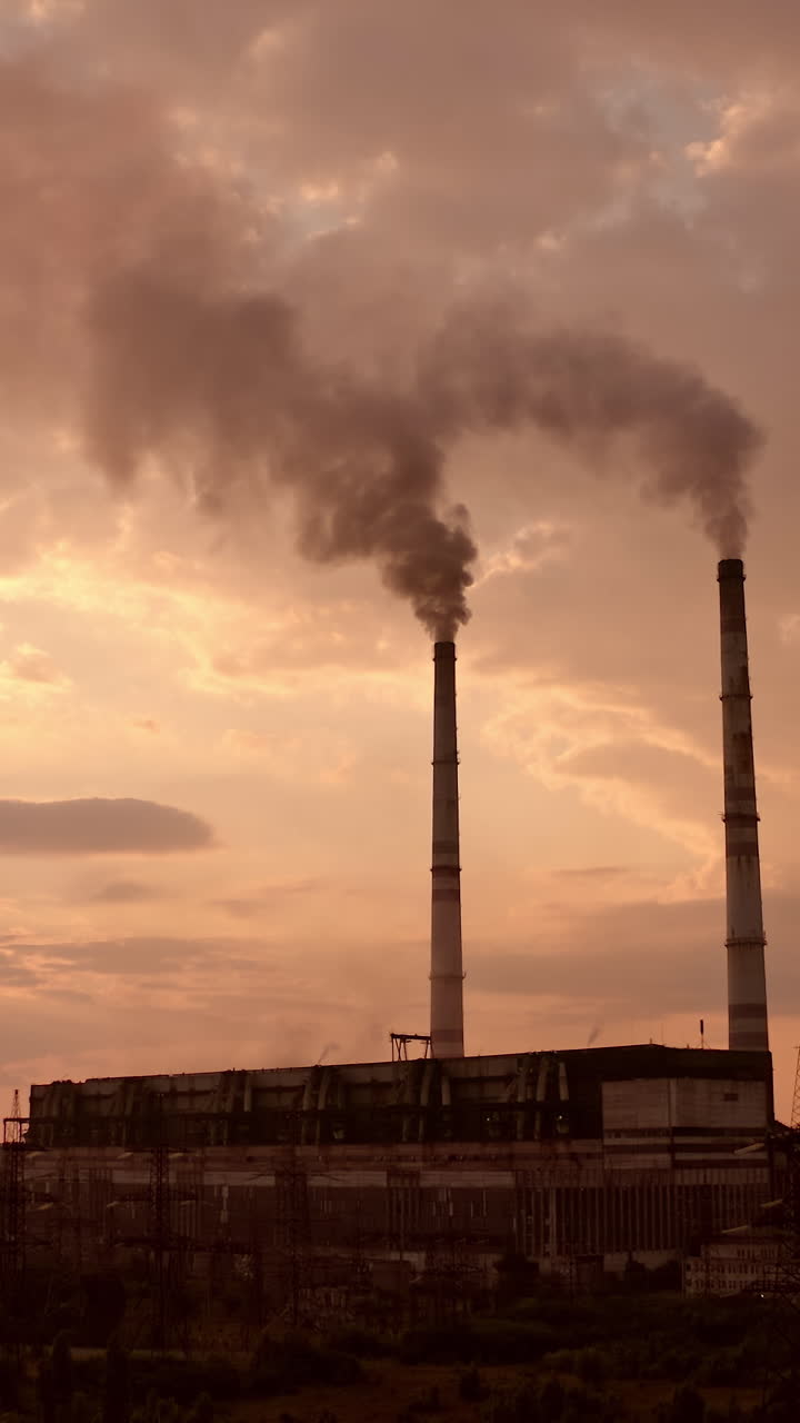 Industrial zone with thick smog from pipes. Factory zone pollutes the atmosphere. Factory chimneys with dirty emissions on the evening sky background. Camera rising. Vertical video