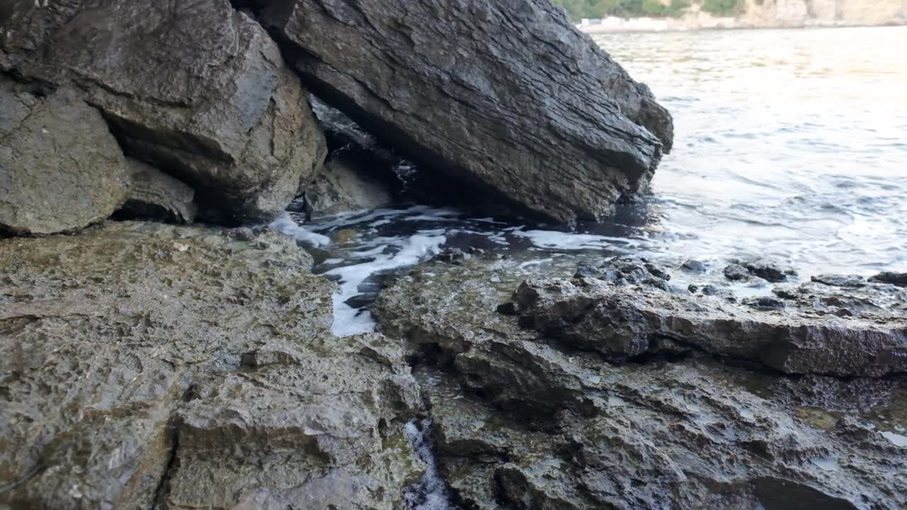Waves crashing into rocks near Budva old town on the coastline of Montenegro on the Adriatic coastline on a sunny sunset afternoon. Slow-motion footage of waves crashing in 4k