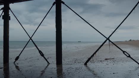 wide shot of the beach from underneath the structure of a seaside pier