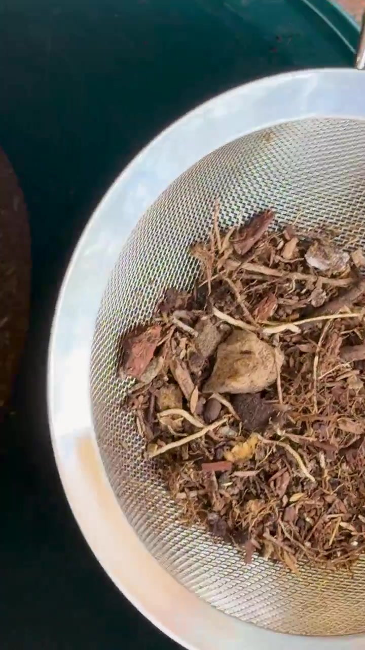 Organic compost sifted with handheld mesh strainer, separating fine soil from debris in outdoor garden