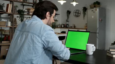 over the shoulder shot of a young businessman typing on laptop with green mockup screen while working at desk in the office