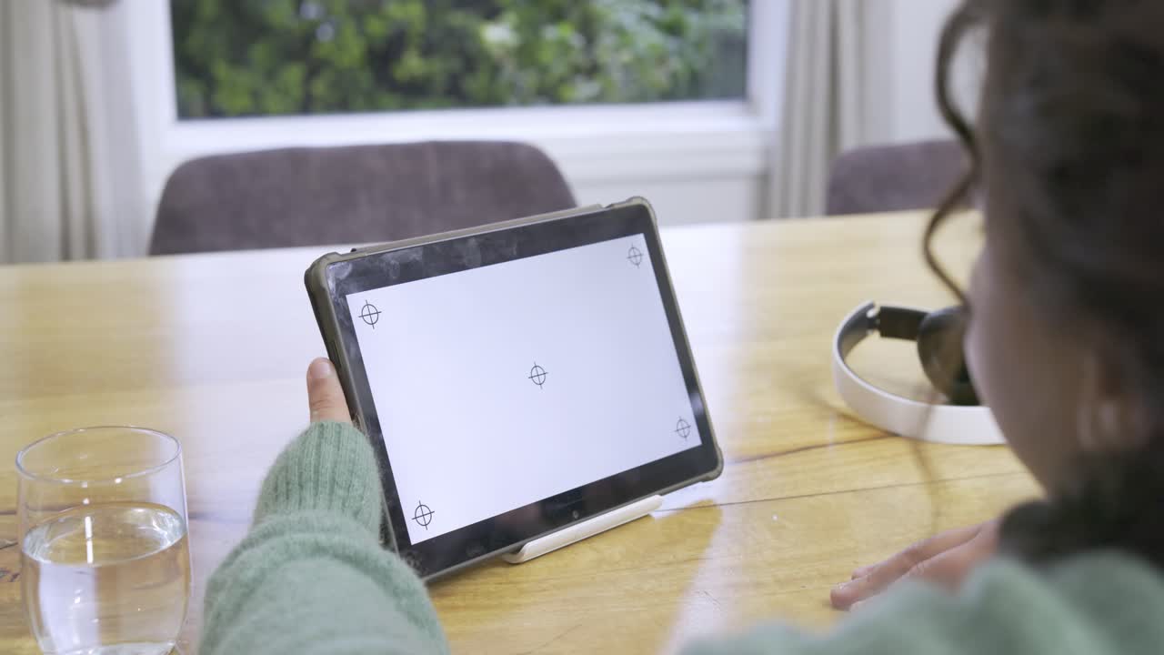 African American child girl reacting to blank screen, tilting tablet at table by window, copy space