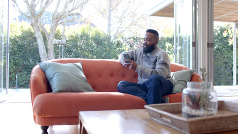 African-american-man-using-smartphone-in-sunny-living-room,-slow-motion