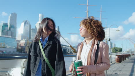 female colleagues walking along city riverbank, smiling and chatting