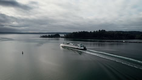 A-Washington-State-ferry-cruises-out-to-open-water,-dark-gloomy-clouds-reflect,-aerial