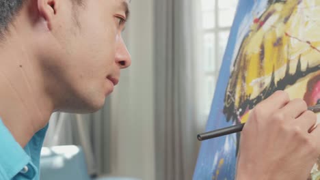 close up side view of an asian artist man holding paintbrush mixed colour and thinking before painting a girl's face on the canvas