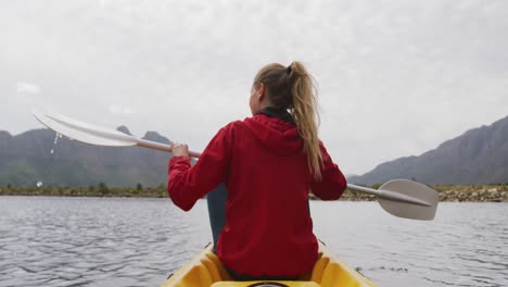 Mujer-Caucásica-Pasando-Un-Buen-Rato-En-Un-Viaje-A-Las-Montañas,-Haciendo-Kayak-En-Un-Lago,-Sosteniendo-Un-Remo