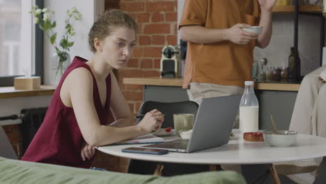 girl having breakfast and working on laptop computer in a shared flat