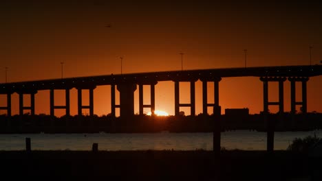 a beautiful sunset under a bridge over water while people walk through the foreground