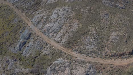 Vista-Panorámica-Aérea-Lenta-A-Través-Del-Paisaje-Con-Camino-De-Tierra-Y-Edificios-A-Lo-Largo-De-él