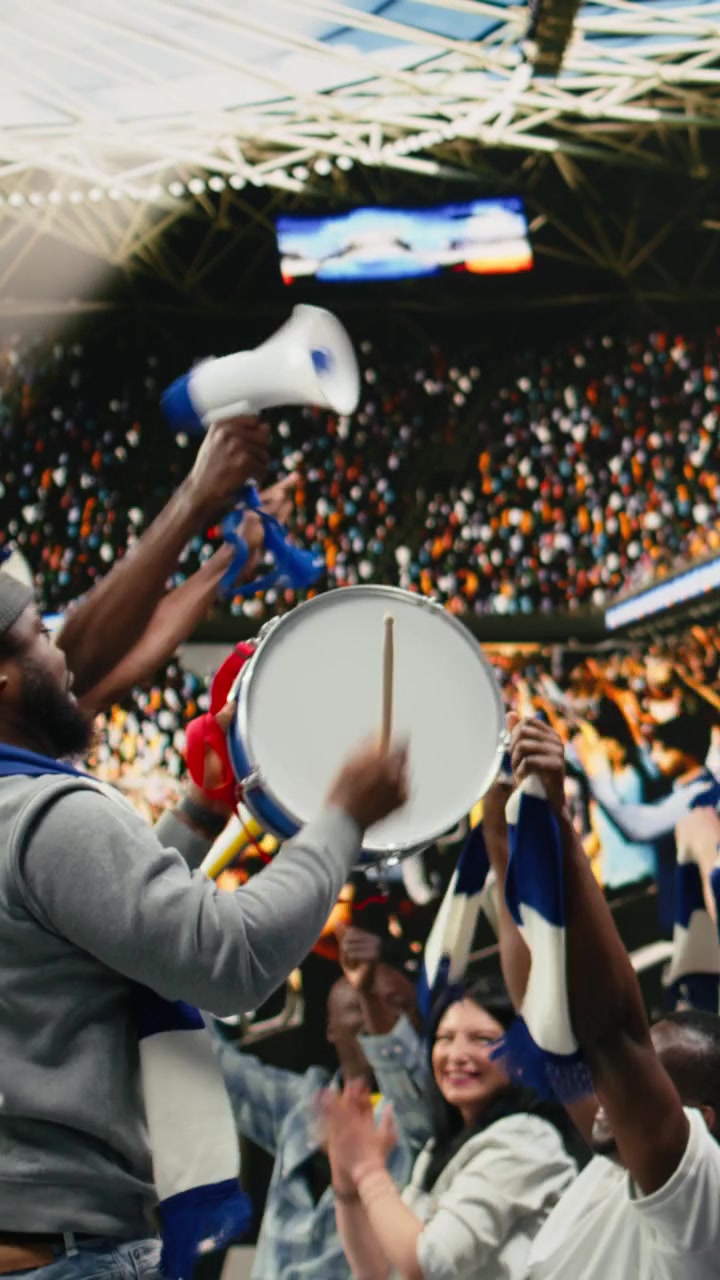 Video vertical: Hinchas de fútbol de raza negra liderando cánticos en un estadio azul con tambor y megáfono