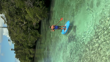 Woman-on-a-paddleboard-in-a-waterway-between-Isle-of-Pines-New-Caledonia-and-Kotomo-Island---vertical-aerial