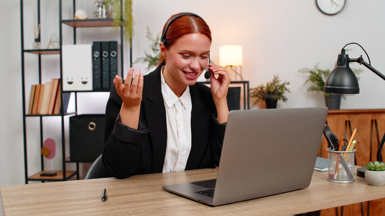 Giovane donna d'affari con cuffie guida una videochiamata con un cliente su un laptop sorridendo e parlando durante l'assistenza