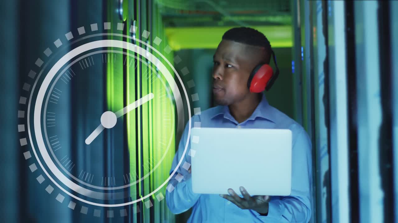Animation of clock over african american man working with laptop and servers