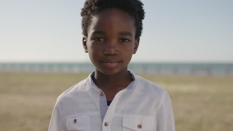 Nahaufnahme-Eines-Porträts-Eines-Süßen-Afroamerikanischen-Jungen,-Der-Ernst-Und-Nachdenklich-In-Die-Kamera-Blickt,-Vor-Dem-Hintergrund-Eines-Strandparks-Am-Meer