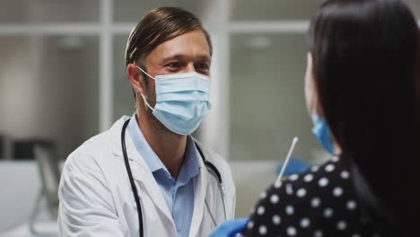 médico caucásico de sexo masculino con máscara facial y guantes tomando una prueba de hisopo del paciente