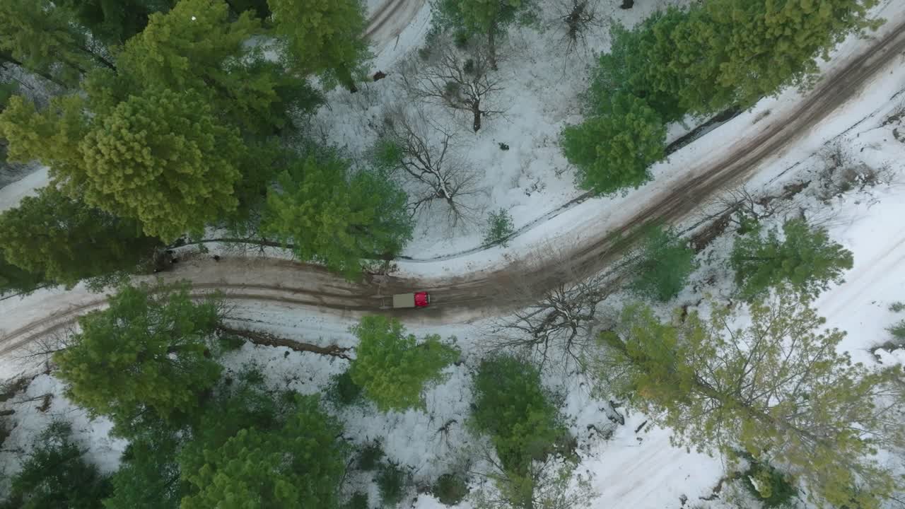 un disparo aéreo captura un coche rojo atravesando una carretera sinuosa rodeada de árboles cubiertos de nieve y terreno