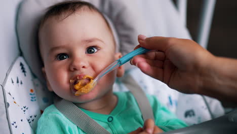 lovely child sitting in a baby chair. mother's hand is feeding her son from a spoon. close up.
