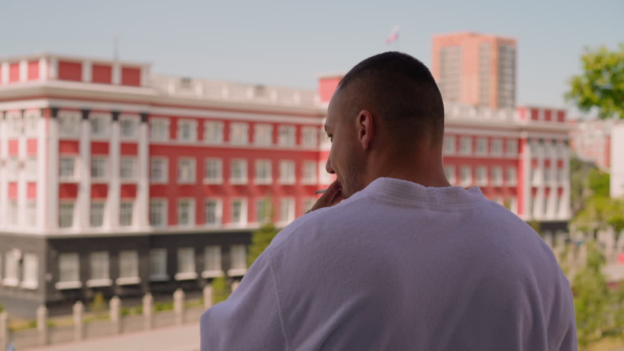 Uomo in accappatoio di spugna fuma sigaretta sul balcone della camera d'hotel