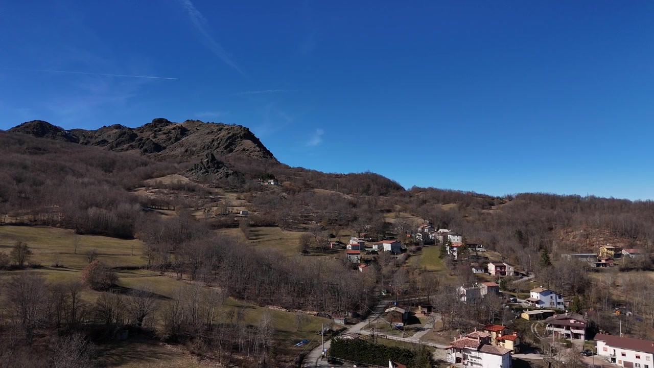 Piccolo borgo rurale vicino a Monte Lama nell'Appennino settentrionale dell'Emilia Romagna, Italia, circondato da boschi di montagna, campi terrazzati e case isolate in collina. Ripresa aerea del paesaggio con drone.