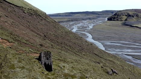 Aerial-of-a-brown-and-green-slope-of-the-mountains-and-wide-riverbed-of-shallow-glacier-river-with-blue-water