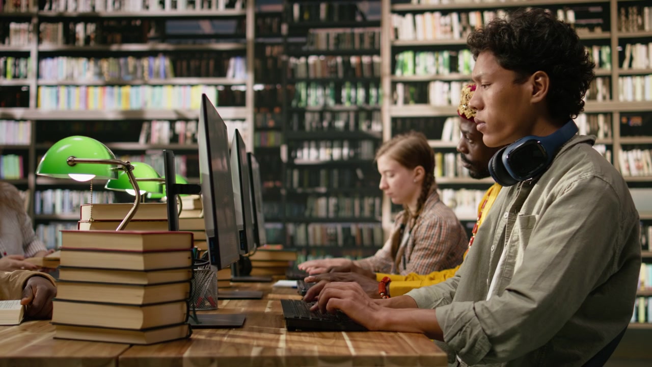 Young adult with headphones around his neck taking notes on computer desktop