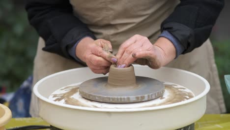 an elderly female craftsman works on a potter's wheel and makes a clay product. hands close-up.