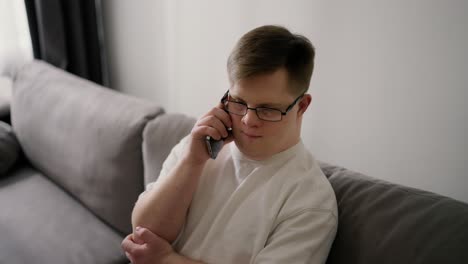 young downs syndrome guy sitting on sofa using mobile phone at home