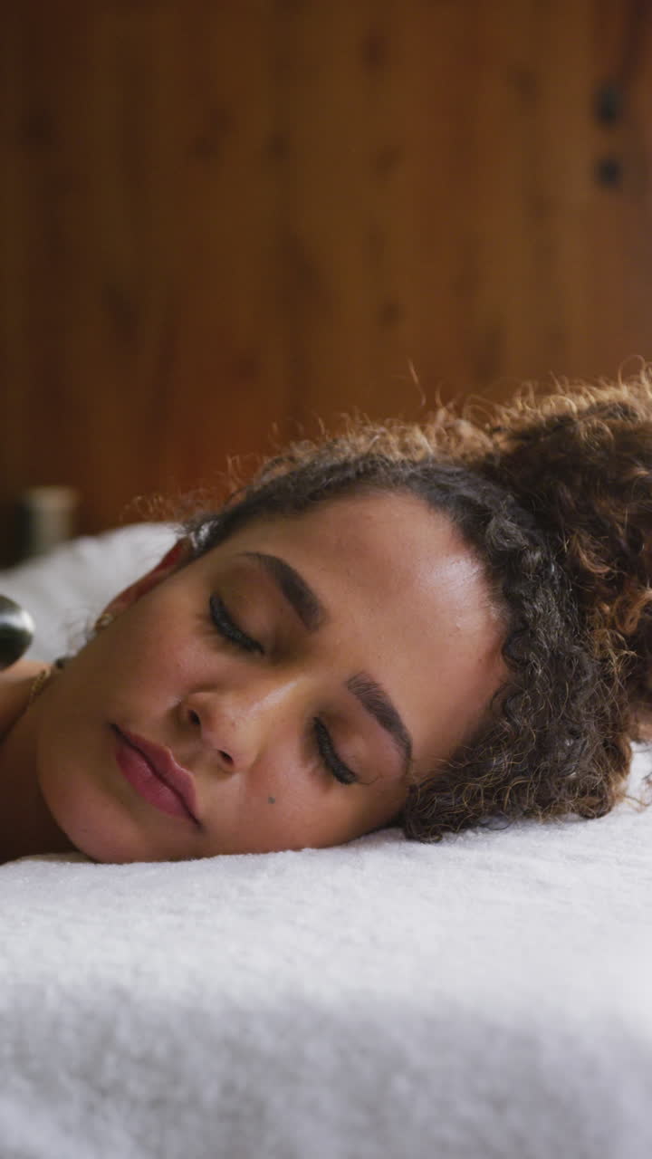 video vertical de una pareja relajada y diversa teniendo un tratamiento de masaje con piedras calientes en un spa de salud