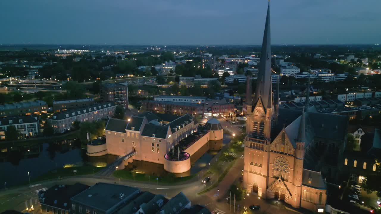 Night aerial view of the illuminated Petrustoren and Petruskerk in Woerden dominating the historic city center with surrounding rooftops and streets