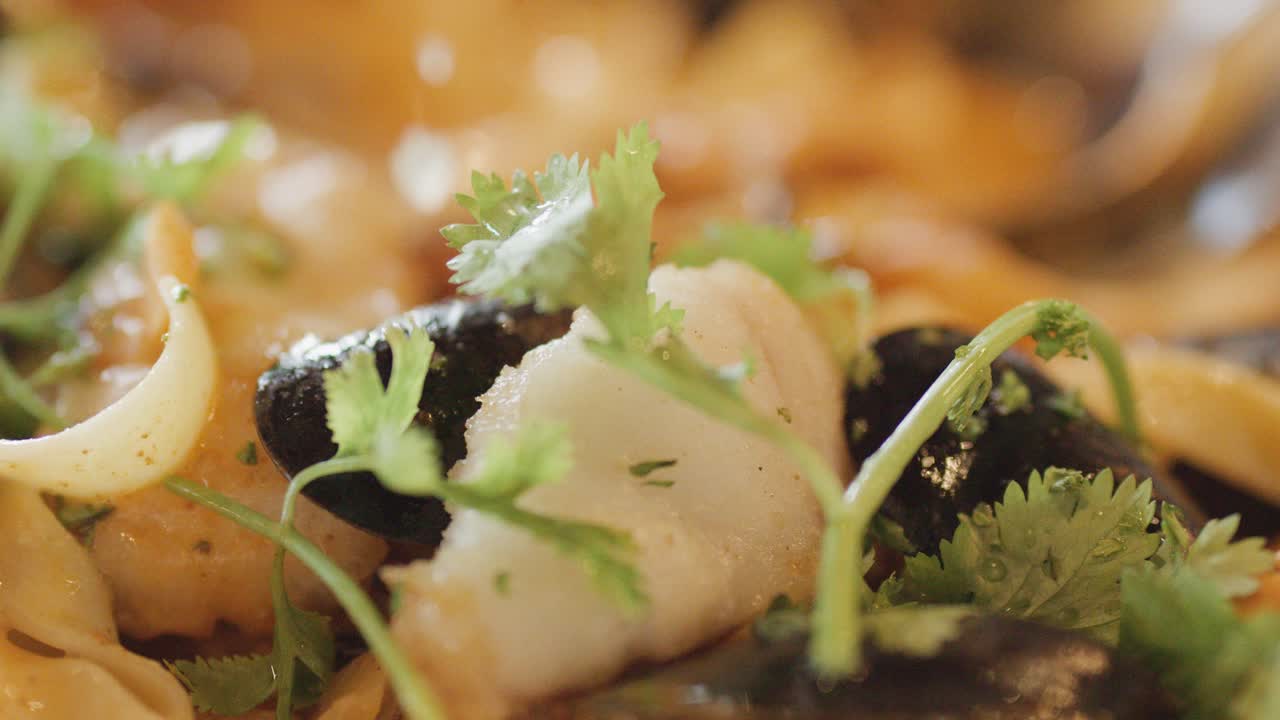 Macro view of assorted seafood including fish, squid, mussels, and scallops in a hot chowder, garnished with fresh herbs under warm, natural lighting