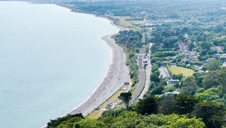 Killiney-Beach-with-a-lot-of-people-on-a-sunny-day,-with-a-train-station-to-the-right-and-full-car-parks,-Ireland