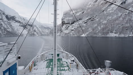 POV-footage-of-a-boat-ride-through-Geirangerfjord,-Norway,-highlighting-the-fjord's-tranquil-beauty-and-the-surrounding-snowy-mountains-in-winter