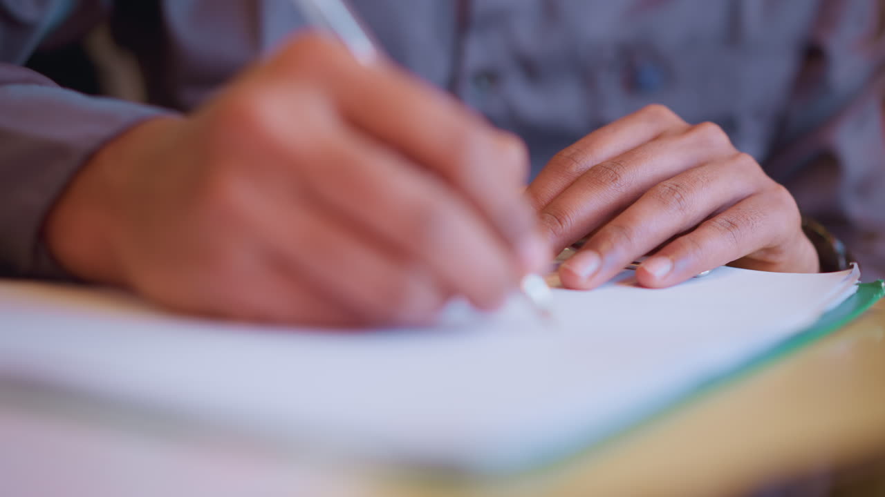 Close-up of hands actively writing on white paper clipped to board, capturing moment of focused handwriting or sketching with pen in calm indoor environment, emphasizing creativity, learning, and productivity