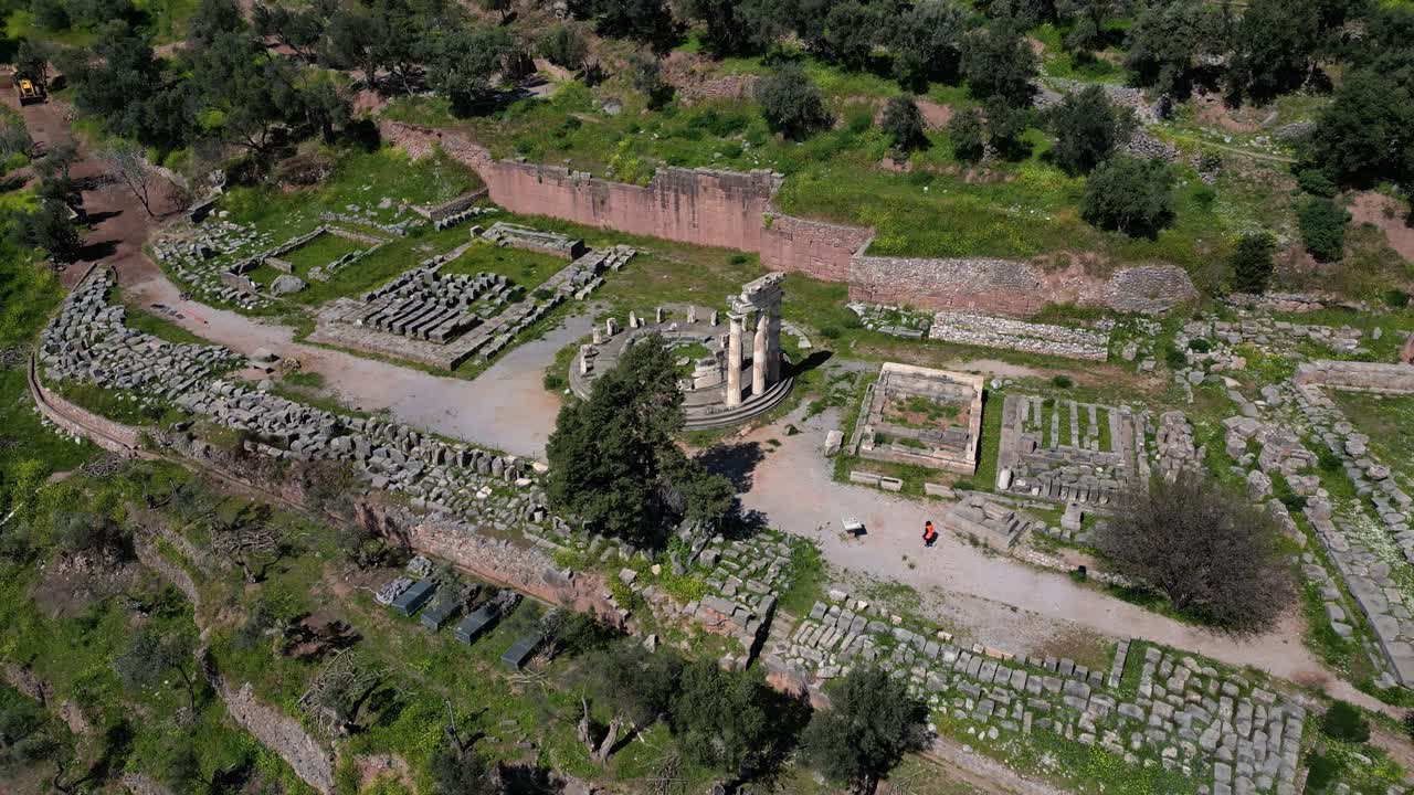 Scenic aerial of Athena Pronaia sanctuary in Delphi with round temple remains and lush hills