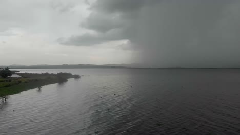 Toma-Aérea-Volando-A-Baja-Altura-Sobre-El-Lago-Victoria-Con-Una-Gran-Tormenta-Que-Cae-Lluvia-En-El-Horizonte