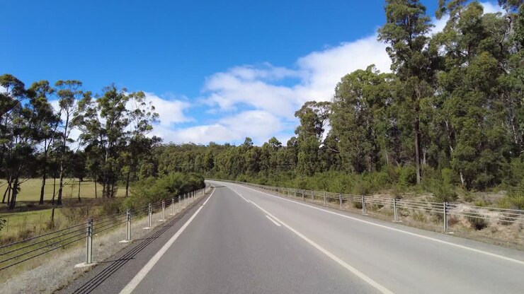 Guidare lungo una strada di campagna in una giornata di sole per un viaggio on the road nella Tasmania rurale